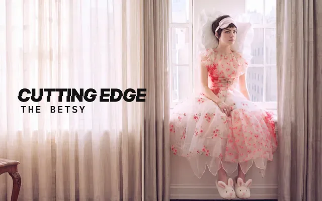 AI-generated image: The Betsy, The Cutting Edge: a woman with a short dark graduated cut and a sleeping mask pushed up like a headband, in a rose organza dress and bunny slippers, sitting on a sunlit apartment windowsill