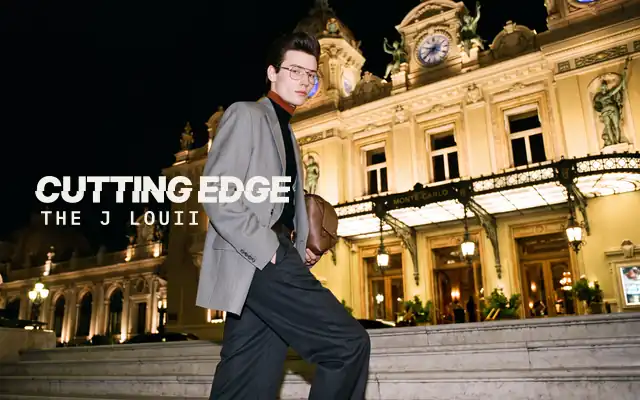 AI-generated image: The J Louii, The Cutting Edge: a young man with a dark swept-back pompadour, grey blazer and gold glasses, on the steps of the Casino de Monte-Carlo at night