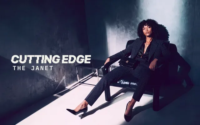AI-generated image: The Janet, The Cutting Edge: a woman with shoulder-length tight spiral curls and a curly fringe, slouched loosely in a black leather lounge chair in a black pinstripe suit and black stilettos, in a dark teal room lit by a soft column of window light