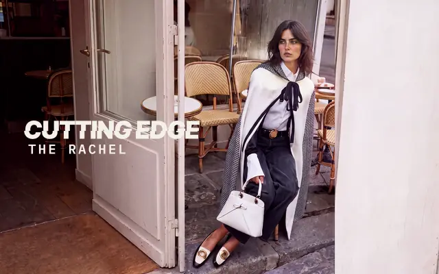 AI-generated image: The Rachel, The Cutting Edge: a woman with a dark shoulder-length layered shag, centre part and no fringe, in an ivory houndstooth-lined cape holding a white handbag, seated on the step of a Paris café doorway